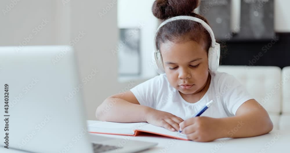 Afro american kid girl school pupil wearing headphones studying online from home watching web class lesson or listening tutor by video call elearning on pandemic isolation. Children remote education. Afro american kid girl school pupil wearing headphones studying online from home watching web class lesson or listening tutor by video call elearning on pandemic isolation. Children remote education.