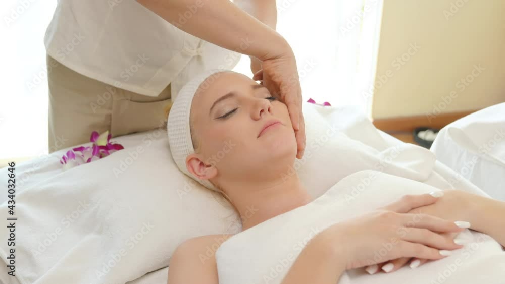 Young beautiful Caucasian woman lying on spa bed get facial massage treatment with aroma essential oil skincare from massage therapist at beauty salon. Wellness health care body massage spa concept. Young beautiful Caucasian woman lying on spa bed get facial massage treatment with aroma essential oil skincare from massage therapist at beauty salon. Wellness health care body massage spa concept.
