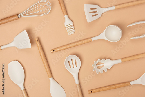 Pattern made from cooking utensil set. Silicone kitchen tools with wooden handle on beige background. Top view Flat lay
