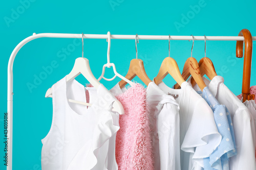 Rack with stylish clothes and umbrella on color background, closeup