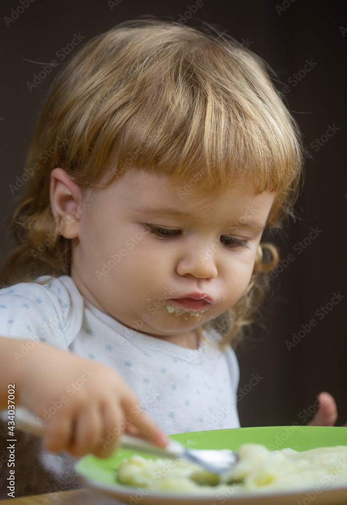 Kid baby with a spoon and a plate in the kitchen at home. Kid baby with a spoon and a plate in the kitchen at home.
