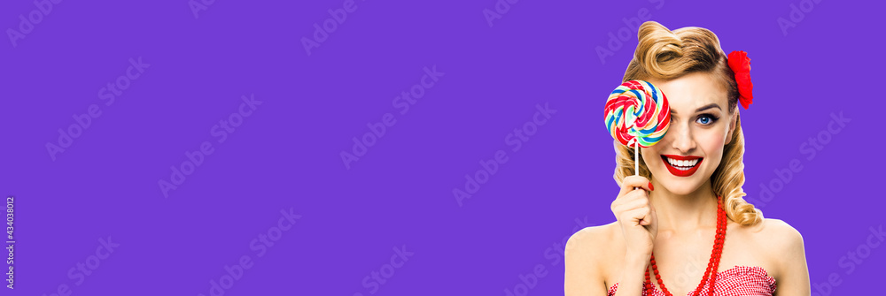 Half face portrait of excited woman with lollipop covering one eye. Pin up girl with happy smile. Retro style image. Violet color background. Ophthalmology concept.