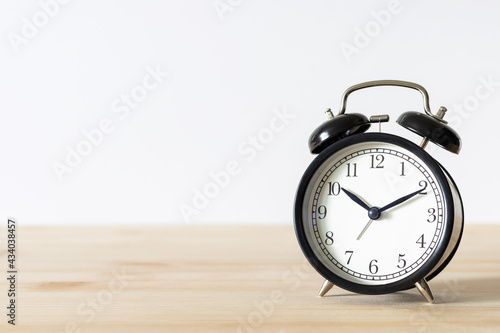 Classic black alarm clock on wooden table with white background and copy space