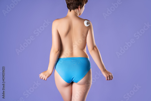 Woman with bare back applying body foam on her shoulder on purple background photo