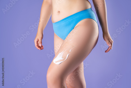 Woman applying anti cellulite foam to thighs on purple background