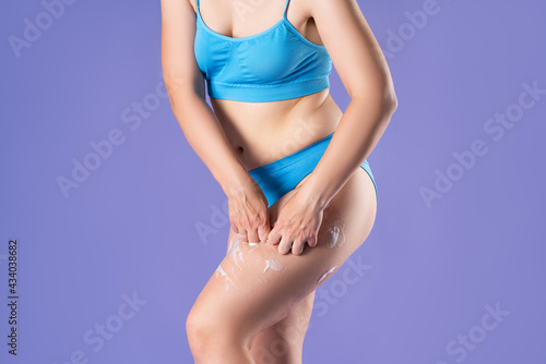 Woman applying anti cellulite foam to thighs on purple background