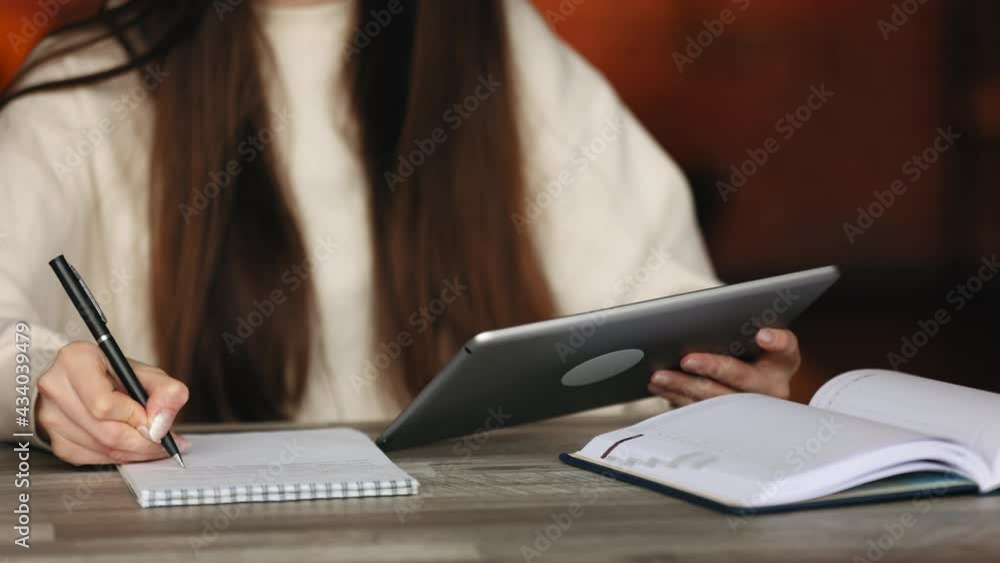 A woman's hands are working with a tablet. She is making notes in her notebook. The woman is sitting at a desk in her home office. Close-up shooting. 4K A woman's hands are working with a tablet. She is making notes in her notebook. The woman is sitting at a desk in her home office. Close-up shooting. 4K