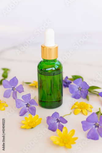 Green cosmetic bottle with pipette on white background with flowers, product packaging, anti aging serum with peptides, cosmetics mockup, spa concept.