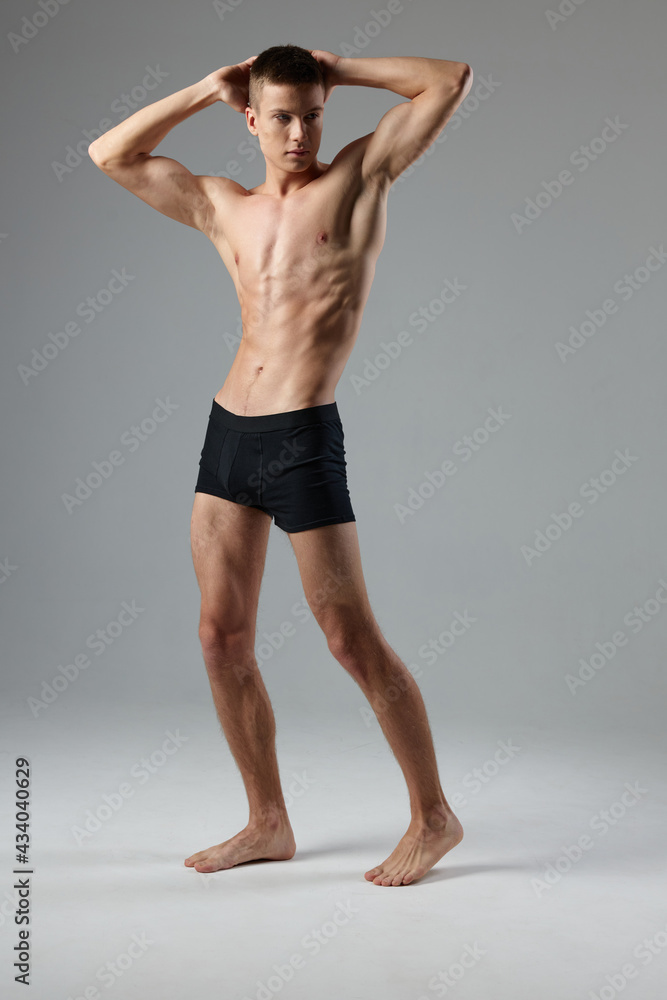 athlete in black shorts holds hands behind his head naked torso gray room full-length model Copy Space
