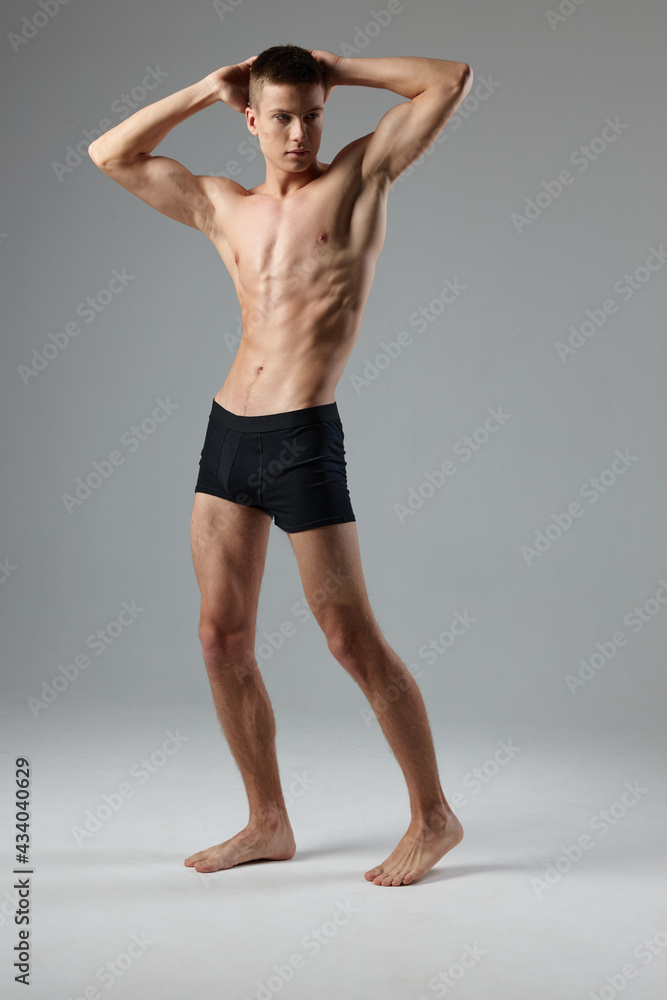 Fototapeta premium athlete in black shorts holds hands behind his head naked torso gray room full-length model Copy Space