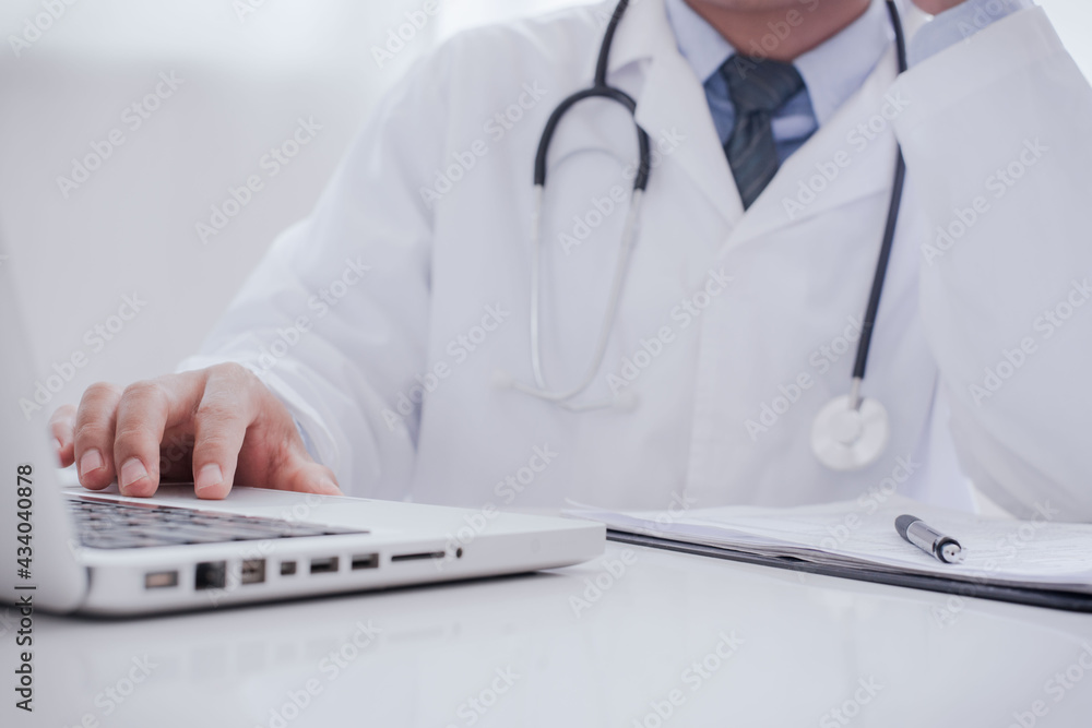 Doctor working with laptop computer and writing on paperwork. Hospital background. Healthcare and medical concept. Focus on stethoscope.. Doctor working with laptop computer and writing on paperwork. Hospital background. Healthcare and medical concept. Focus on stethoscope..