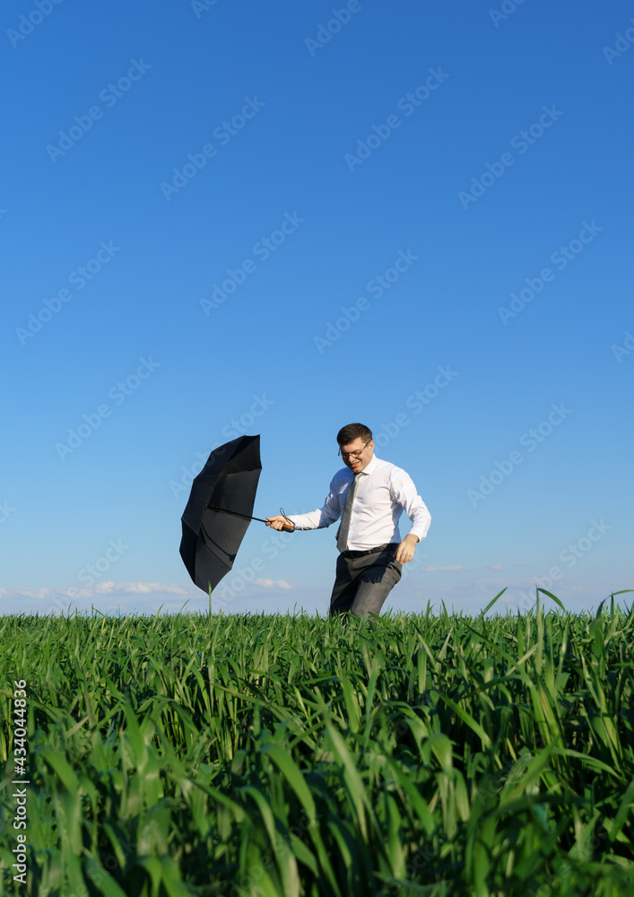 businessman walks with umbrella in a field, green grass and blue sky as background