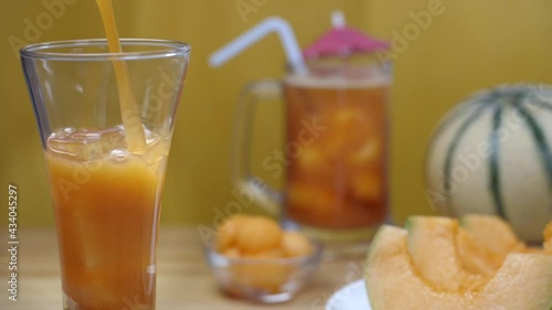 Pouring of healthy drink with fruit slices and ice cubes - nutritious food.  Summer drink India. Closeup shot of yellow sliced Kharbuja on a plate with a cocktail juice decorated with an umbrella k... photo