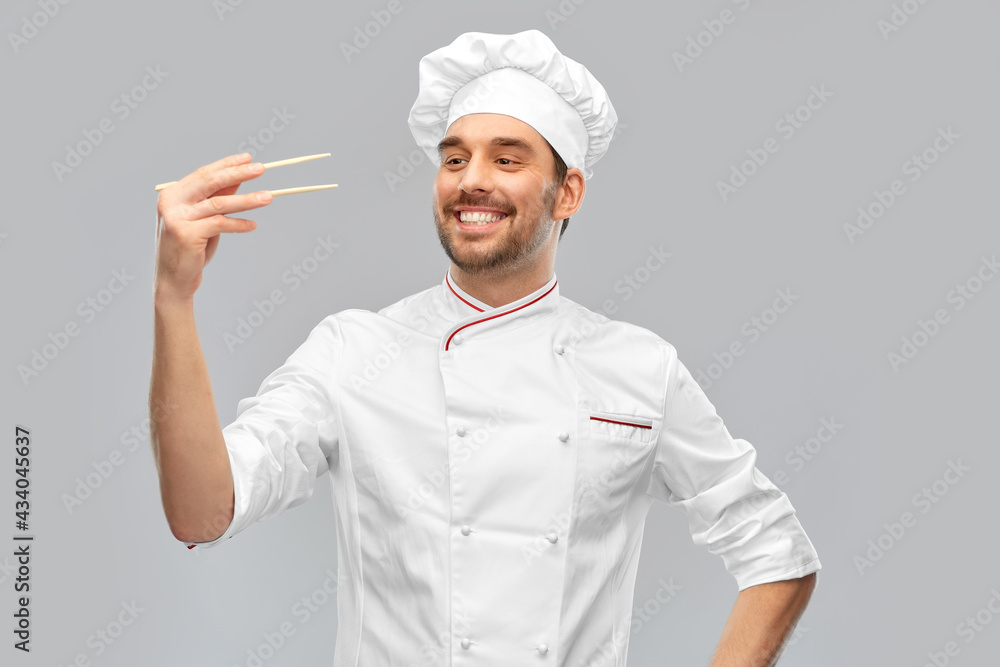 food cooking, asian cuisine and people concept - happy smiling male chef in toque holding something with chopsticks over grey background food cooking, asian cuisine and people concept - happy smiling male chef in toque holding something with chopsticks over grey background