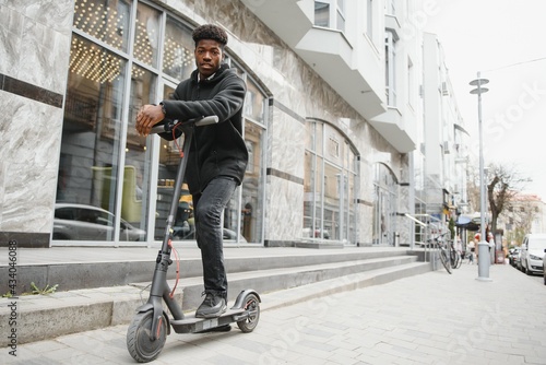 afro american guy rides an electric scooter against the background of a wall, a student uses eco transport