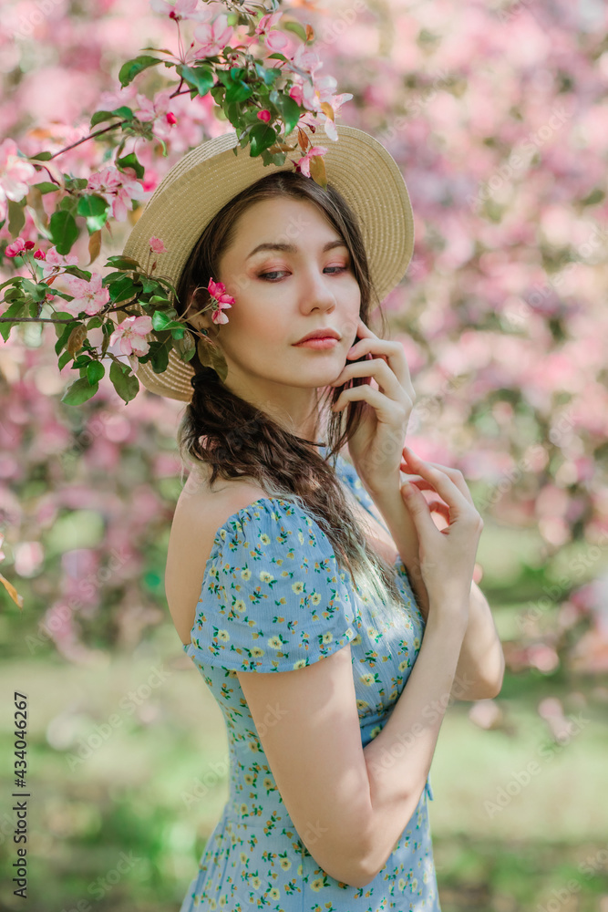Φωτογραφία Portrait of nice young girl holding straw hat in front of blooming apple garden