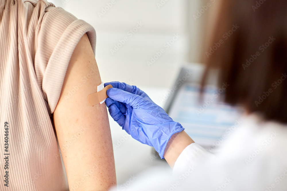 health, medicine and vaccination concept - close up of doctor attaching adhesive medical plaster or patch to patient at hospital