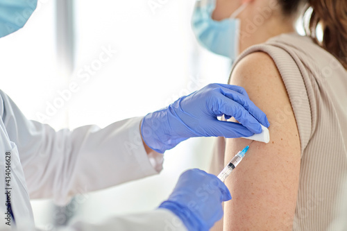 health  medicine and pandemic concept - close up of female doctor or nurse wearing protective medical gloves with syringe vaccinating patient at hospital