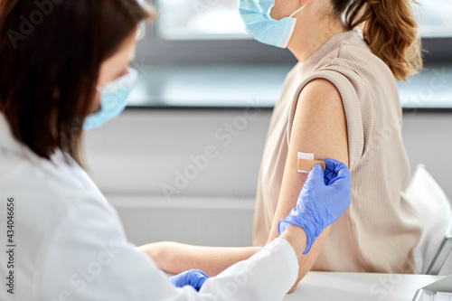 health, medicine and vaccination concept - close up of doctor wearing protective medical mask and gloves attaching adhesive medical plaster or patch to patient at hospital