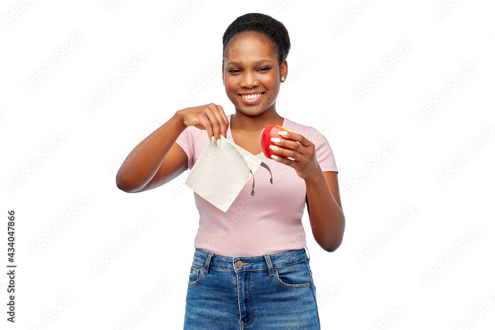 sustainability, eco living and people concept - portrait of happy smiling young african american woman putting apple into reusable bag over grey background sustainability, eco living and people concept - portrait of happy smiling young african american woman putting apple into reusable bag over grey background