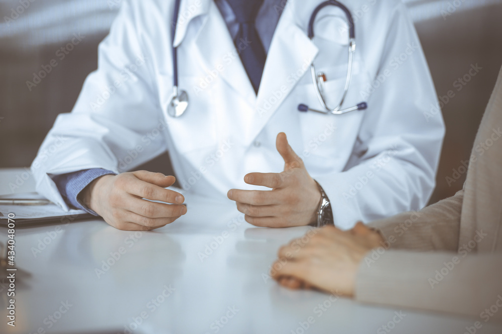 Unknown male doctor and patient woman discussing something while sitting in clinic and using clipboard. Best medical service in hospital, medicine, pandemic stop Unknown male doctor and patient woman discussing something while sitting in clinic and using clipboard. Best medical service in hospital, medicine, pandemic stop