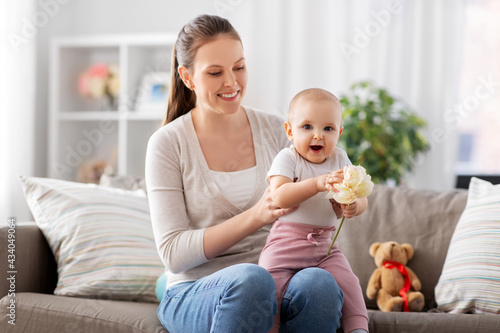 family, motherhood and people concept - happy smiling mother and little baby daughter playing with flower at home