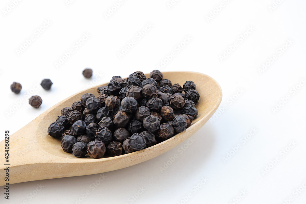 Wooden spoon and black pepper grains on white background. Wooden spoon and black pepper grains on white background.