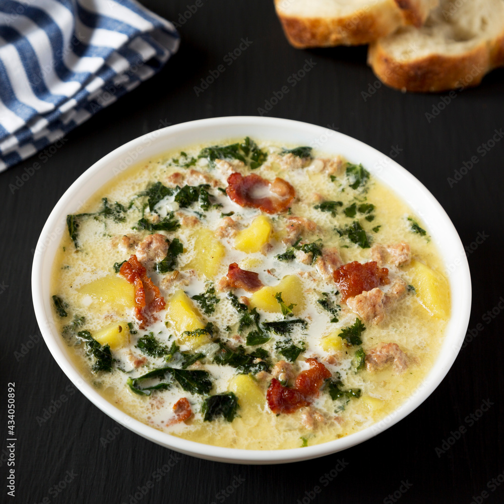 Homemade Zuppa Toscana with Kale and Bread in a white bowl on a black background, side view.