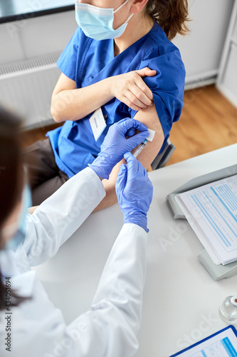 health, medicine and pandemic concept - female doctor or nurse wearing protective medical mask and gloves with syringe vaccinating medical worker hospital