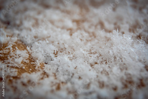 Tiny white snowflakes on a piece of wood. Closeup of snow pattern. Macro photography of geometric texture. Selective focus on the flakes, blurred background.