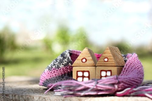 pair of wooden houses wrapped together in a warm scarf on a blurred landscape background. cozy locked family home