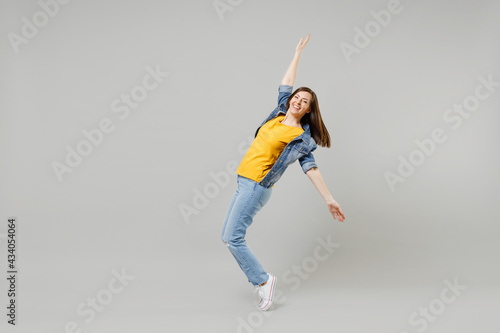 Fototapeta Naklejka Na Ścianę i Meble -  Full length side view young caucasian woman in casual denim jacket yellow tshirt looking camera leaning back stand on toes dancing isolated on grey background studio portrait People lifestyle concept
