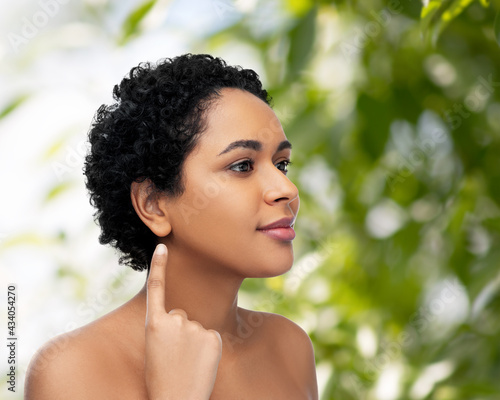 hearing, health and beauty concept - portrait of happy smiling young african american woman with bare shoulders showing her ear over green natural background photo