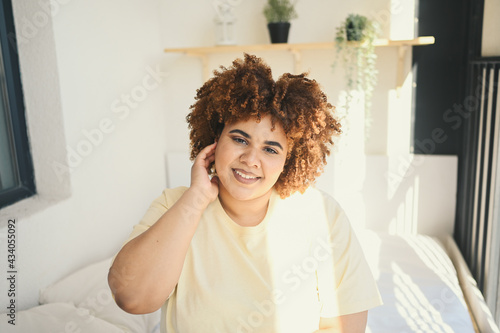 Beautiful happy curvy plus size African black woman afro hair posing in beige t-shirt and underwear on sunny balcony bedroom. Body imperfection, body acceptance, body positive and diversity concept.