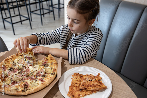 The little girl takes a slice of delicious pizza.