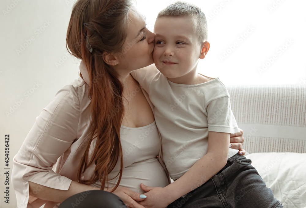 A young pregnant woman is kissing her little son. A young pregnant woman is kissing her little son.