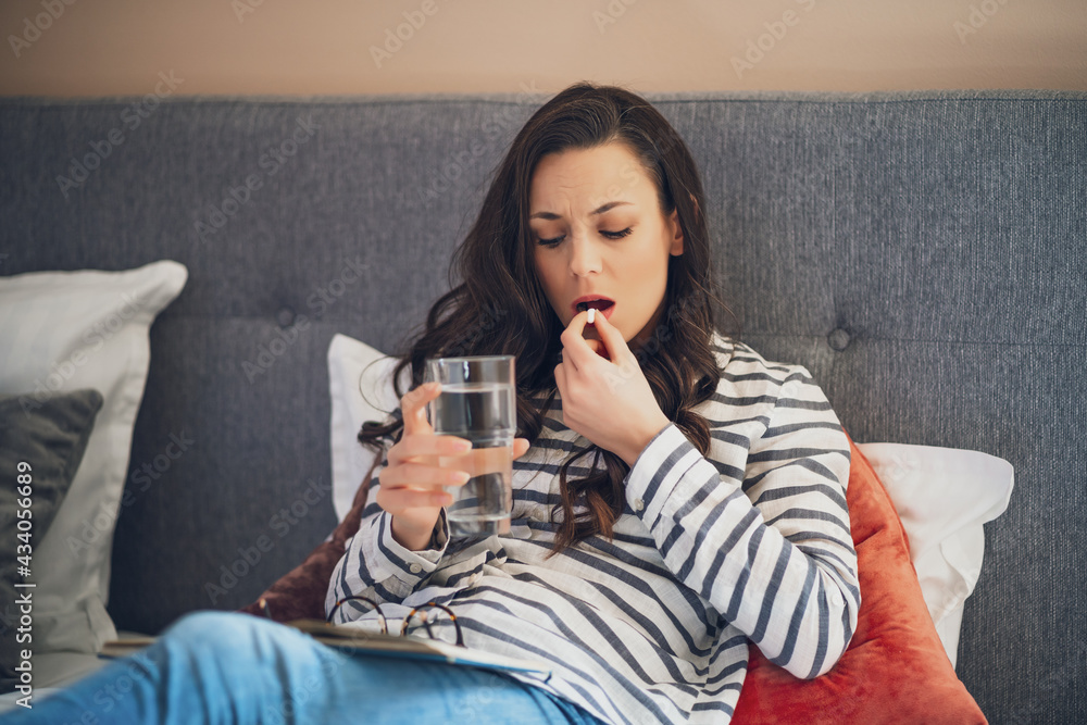 Young woman is lying in bed in her home. She is sick and talking pill. Young woman is lying in bed in her home. She is sick and talking pill.