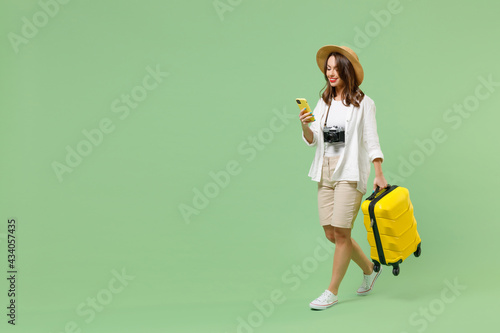 Full length traveler tourist woman in casual clothes hat hold suitcase mobile cell phone booking taxi hotel walk isolated on green background Passenger travel abroad weekend Airflight journey concept