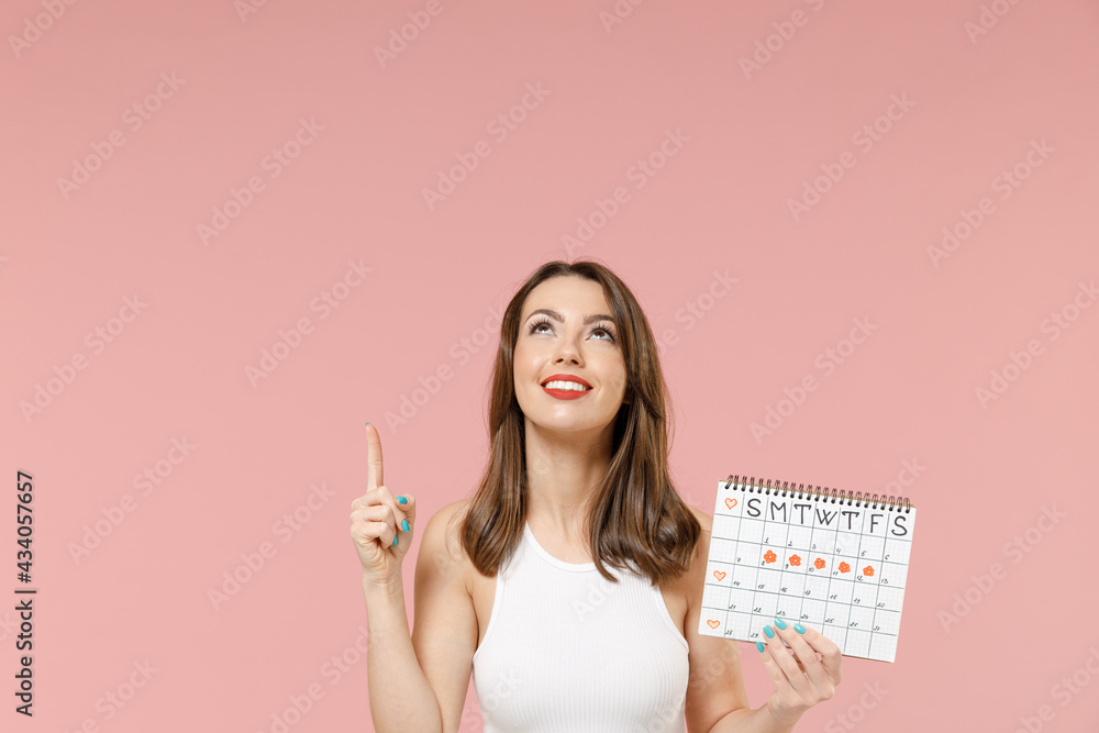 Young woman in white clothes hold female periods calendar checking menstruation day point index finger overhead on mock up area isolated on pink background Medical healthcare gynecological concept Young woman in white clothes hold female periods calendar checking menstruation day point index finger overhead on mock up area isolated on pink background Medical healthcare gynecological concept
