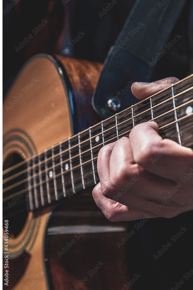 Guitarist playing acoustic guitar in the dark close up.