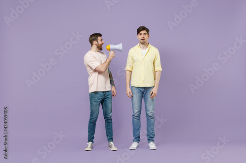 Full length shocked confused disappointed young men friends together in t-shirt scream hot news in megaphone fooling around isolated on purple background studio. People lifestyle friendship concept