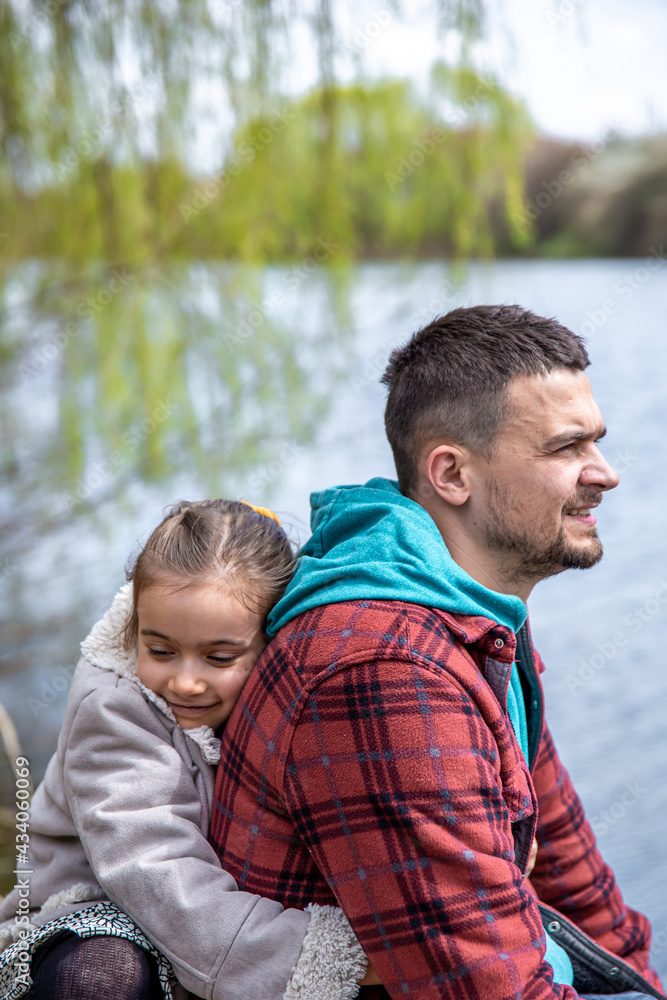 Little girl hugs dad, sitting on the background of the river. Little girl hugs dad, sitting on the background of the river.