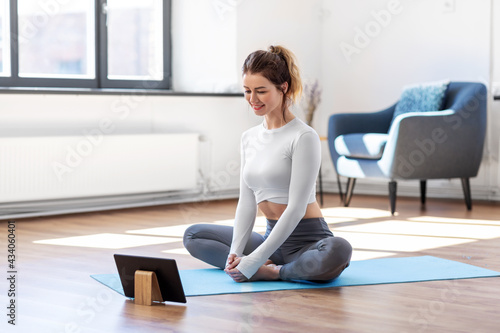 fitness, people and healthy lifestyle concept - young woman with tablet pc computer doing yoga at home