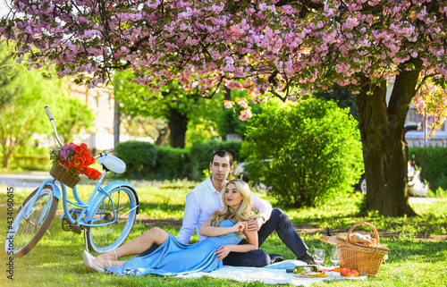 Loving relationship. couple in love on green grass. enjoying nature together. having picnic in city park. man and woman relax with food basket. Romantic traveler couple under sakura blossom tree