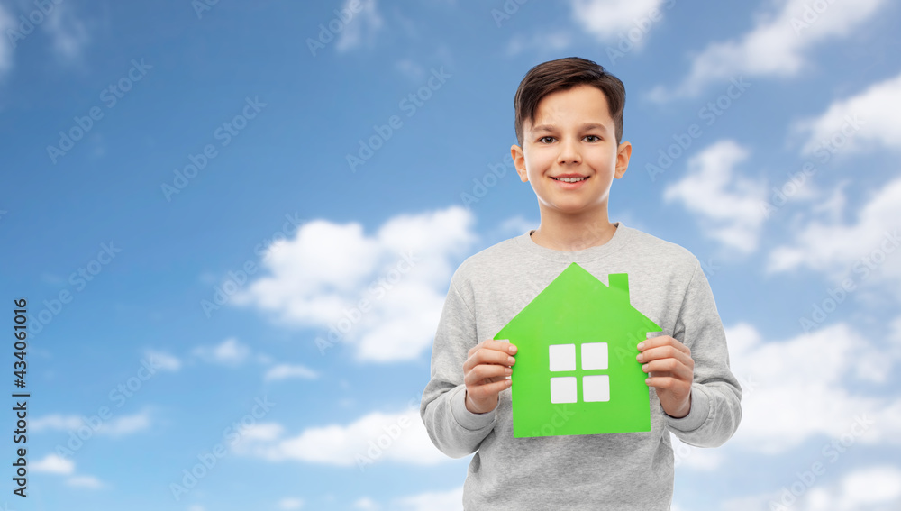 eco living, environment and sustainability concept - smiling boy holding green house icon over blue sky and clouds on background eco living, environment and sustainability concept - smiling boy holding green house icon over blue sky and clouds on background
