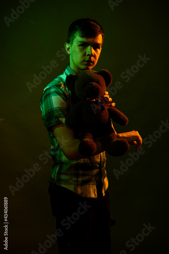 The guy plays with a teddy bear, illuminated by yellow and green light