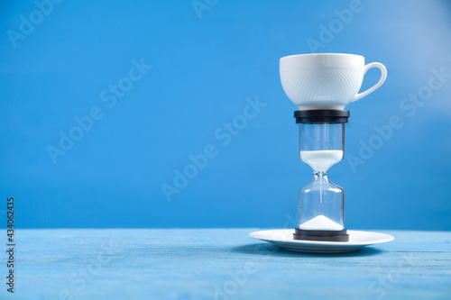 Hourglass and coffee cup on the blue background.