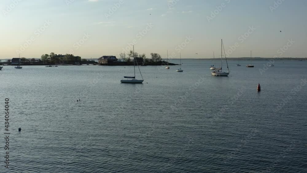 A low altitude drone shot over calm waters, as the camera dolly in and pan left towards some anchored boats and an island, taking in this sunny, peaceful morning. A low altitude drone shot over calm waters, as the camera dolly in and pan left towards some anchored boats and an island, taking in this sunny, peaceful morning.