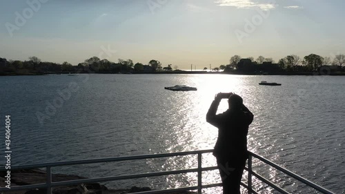 Wallpaper Mural A low angle drone shot over the silhouette of a person standing on a balcony taking a picture of the sunrise. The camera dolly in over the person, towards the calm waters with anchored boats. Torontodigital.ca