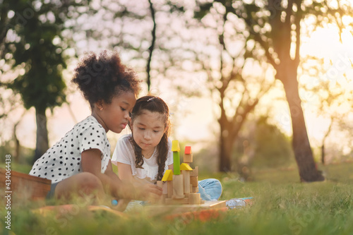 Happy cheerful ethnic girls play wooden block puzzle together at outdoors park , Relationship little kids, Diverse ethnic concept.